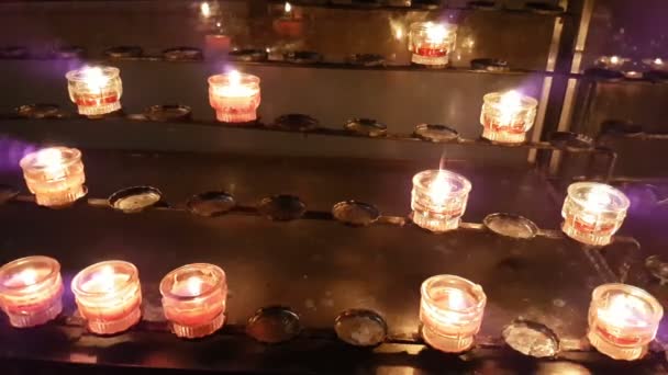 Votive candles lit in some cathedral and standing on some low racks — Stock Video