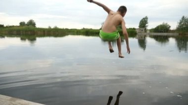 Genç çocuk bir gölde ağır çekimde yaz aylarında ahşap köprüden atlar