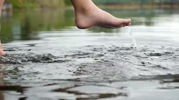 Las piernas femeninas deportivas se balancean tocando el agua en un lago de una manera relajada — Vídeo de stock