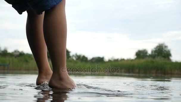 Las piernas delgadas femeninas se balancean tocando el agua en un lago en cámara lenta — Vídeos de Stock