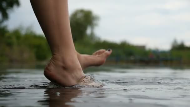 Las piernas delgadas femeninas se balancean, tocando el agua en un lago de una manera relajada — Vídeo de stock