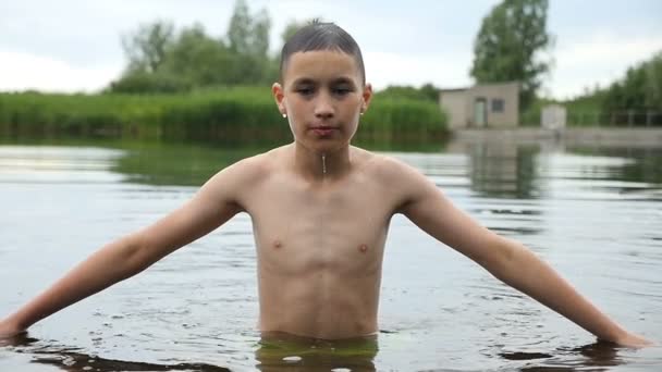 El niño mantiene las manos a un lado y toca el agua en un lago. Se zambulle en cámara lenta — Vídeo de stock