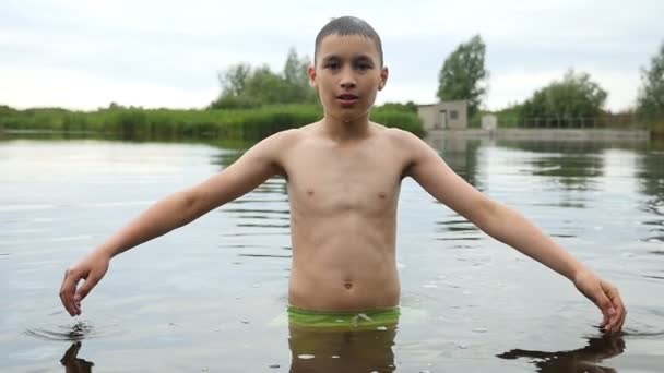 Νεαρό αγόρι κρατά τα χέρια άκρη και αγγίζει το νερό σε μια λίμνη. Πέφτει σε αργή κίνηση — Αρχείο Βίντεο