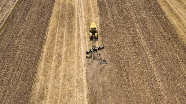 Aerial shot of an agricultural field and a yellow tractor pulling a harrow in spring Stock Photo