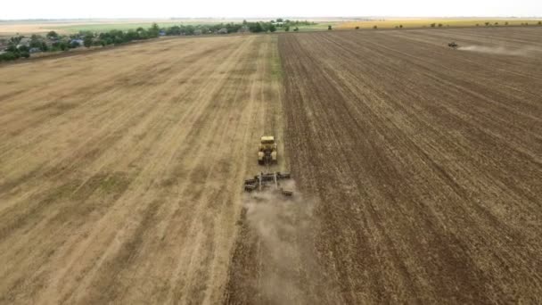 Tiro aéreo de um campo rural e um trator de fazenda que puxa uma grade no verão — Vídeo de Stock