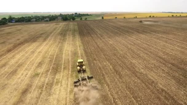 Antenn skott av ett vetefält och en kraftfull traktor som drar en harrow i sommar — Stockvideo