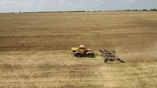 Foto aérea de un vasto campo y un gran tractor tirando de una grada en verano — Vídeo de stock