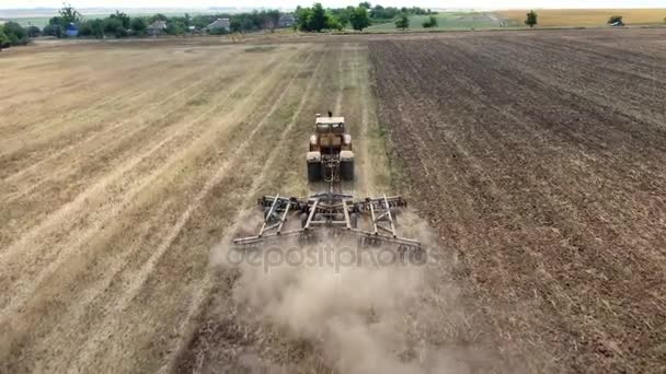 Tiro aéreo de um campo de trigo e um grande trator que puxa uma grade no verão — Vídeo de Stock