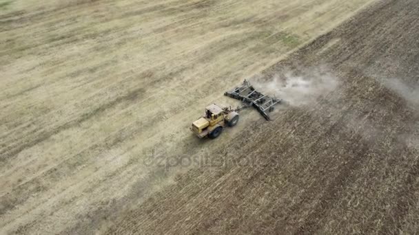 Tiro aéreo de um campo de trigo e um trator potente que puxa uma grade no verão — Vídeo de Stock