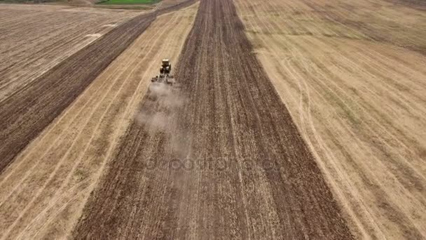 Aerial shot of a boundless field and a big tractor pulling a harrow in summer — Stock Video