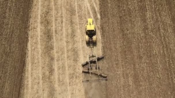 Luchtfoto van een grenzeloze tarweveld en een tractor trekken een harrow in de zomer — Stockvideo