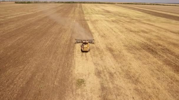 Aerial shot of an agricultural field and a yellow tractor pulling a harrow — Stock Video