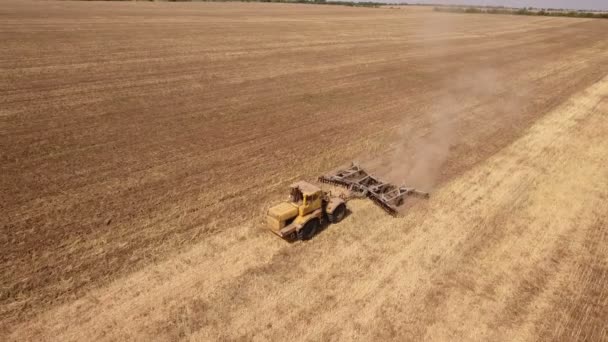 Colpo aereo di un ex campo di grano e di un grosso trattore che tira un erpice in autunno — Video Stock