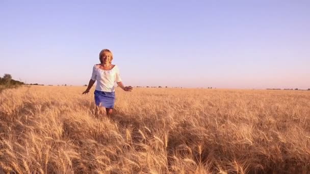 Glimlachend jonge vrouw loopt langs een tarweveld in Oekraïne in de zomer in slow motion — Stockvideo