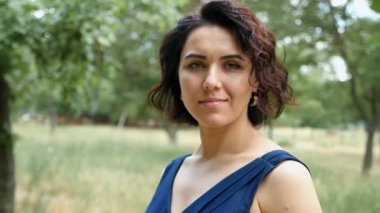 Genç kadın gülümsüyor içtenlikle bir çim yeşil ağaçlar güneşli bir günde slo-mo ile