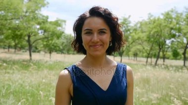 Genç esmer gülümser içtenlikle bir çim yeşil ağaçlar güneşli bir günde slo-mo ile