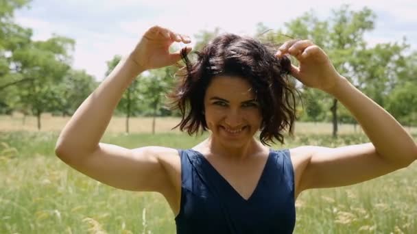 Jonge vrouw staat en werpt haar haar romantisch op een gazon in de zomer in slo-mo — Stockvideo