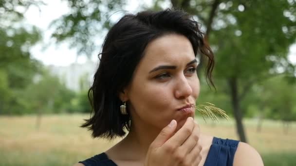 Jonge vrouw neemt een wild gras in haar mond en denkt over iets in slo-mo — Stockvideo