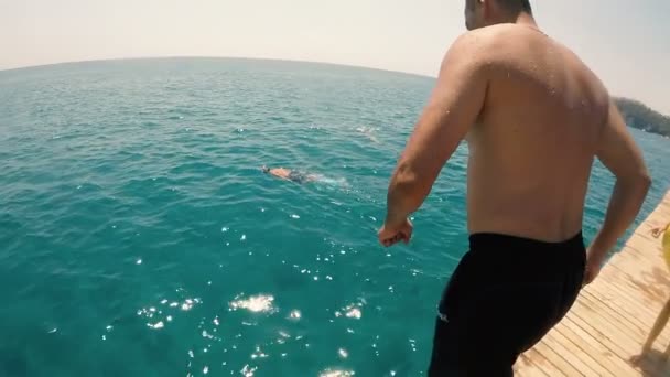 Man jumps in the sparkling sea water from a pier and dissappears there in slo-mo — Stock Video