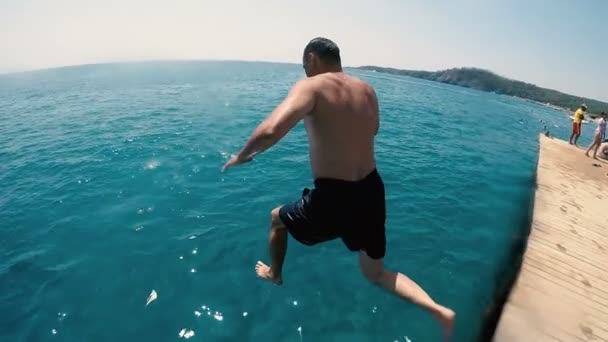 Mężczyzna skacze do wody morza od molo i porusza się powoli pod wodą w slo-mo — Wideo stockowe