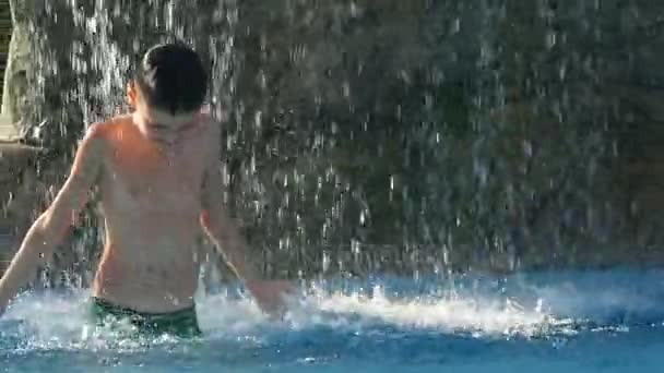 小男孩跳舞在游泳池下喷泉，在炎热的夏天一天得到极大的乐趣 — 图库视频影像
