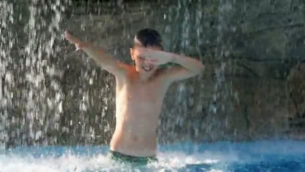 Niño pequeño bailando en la piscina bajo la fuente, consiguiendo un gran placer en un día caluroso de verano — Vídeos de Stock