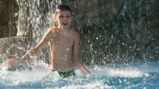 Menino dançando na piscina sob a fonte, obtendo grande prazer em um dia quente de verão, ao ar livre — Vídeo de Stock