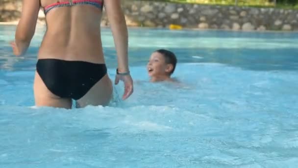 Menino com sua mãe espirra feliz na piscina do parque aquático — Vídeo de Stock
