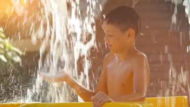 Caluroso día de verano el niño se enfría bajo los arroyos frescos de la cascada en el parque acuático — Vídeos de Stock