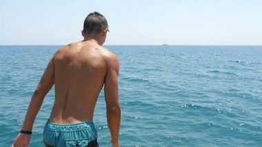 Genç adam çalışır ve ayak ilk yavaş denize bir platformdan diğerine atlar