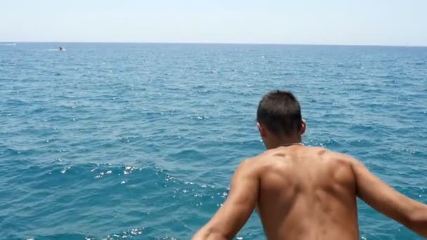 Hulk chico se sumerge directamente desde una plataforma en el mar en verano en cámara lenta — Vídeo de stock