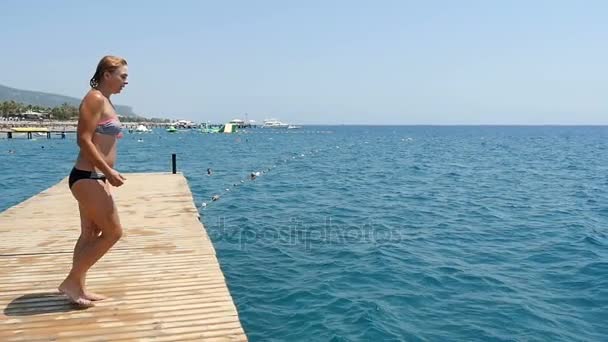 Junge Frau springt im Sommer in Zeitlupe von einer Plattform ins Meer — Stockvideo