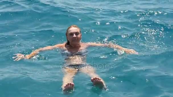 Jonge blonde vrouw zwemt rugslag en glimlacht in de Egeïsche zee in slow motion — Stockvideo