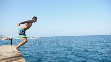 Genç bir adam bir iskeleden slo-mo köpüklü Türkiye Deniz beldesinde içine atlar