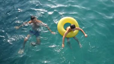 Genç adam ve bir çocuk bir şişme ringde slo-mo mavi deniz sularında yüzmek
