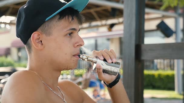 Jovem guarda seu e-cigarro e bebe água em um pub no verão em slo-mo — Vídeo de Stock