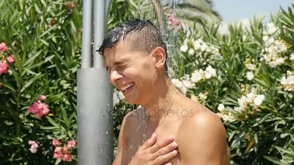 A happy young man takes a shower on a seacoast in summer in slow motion — Stockvideo