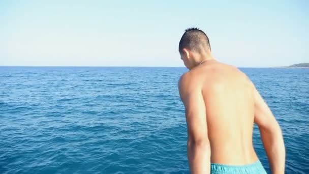 Молодой человек в шортах прыгает в морскую воду с пирса летом в замедленной съемке — стоковое видео