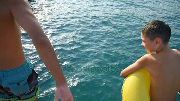 Dos hermanos, grandes y pequeños, saltan los pies primero en las aguas del mar en verano en slo-mo — Vídeo de stock