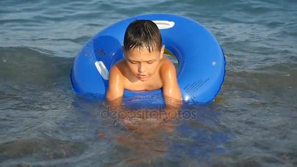 Menino pequeno nada em um anel inflável azul nas águas do mar no verão em slo-mo — Vídeo de Stock