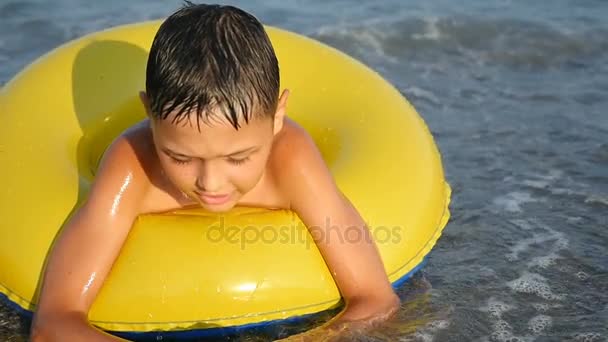 Kleine jongen zwemt in een gele opblaasbare ring in de zee in de zomer in slow motion — Stockvideo