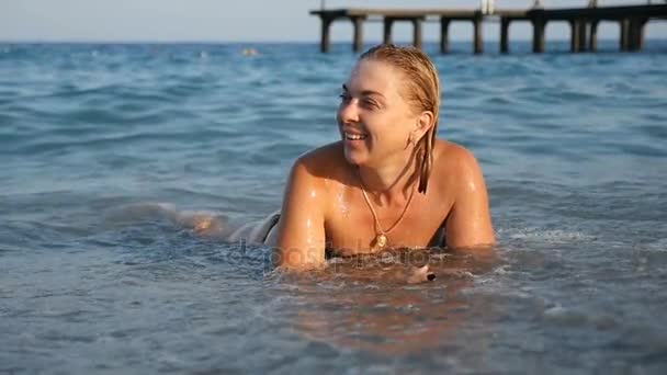 Vrolijke jonge vrouw liggend in het blauwe water van de zeekust in de zomer in slo-mo — Stockvideo