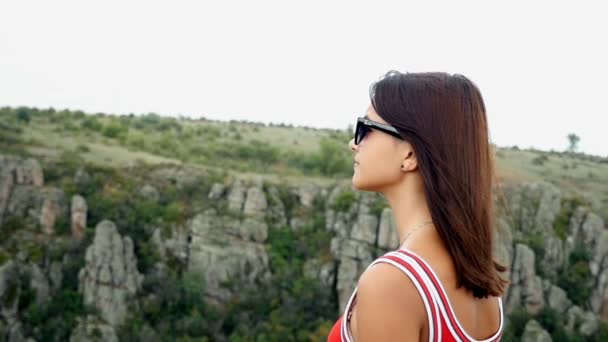 An attractive girl stands in profile atop of a high cliff in summer in slow motion — Stock Video