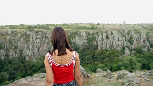 A slim girl goes to an edge of a high cliff in summer in slow motion — Stock Video