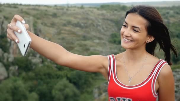 Niza chica en vestido rojo toma una selfie en la cima de un acantilado cerca de un abismo en slo-mo — Vídeo de stock