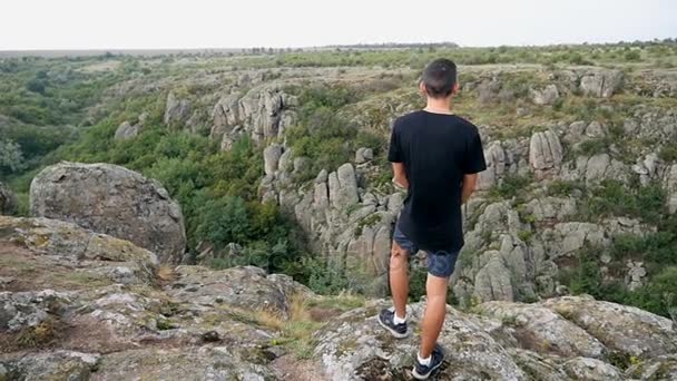 Un hombre fuerte se para en la cima de un acantilado mirando colinas peligrosas en slo-mo — Vídeos de Stock