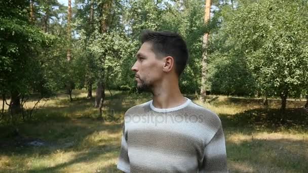 Een jonge man kijkt opzij op een zonnig grasveld in een dennenbos in de zomer in slo-mo — Stockvideo