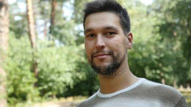 Genç bir beyaz adam bir çam ormanı ve ağır çekimde mutlulukla gülümser duruyor