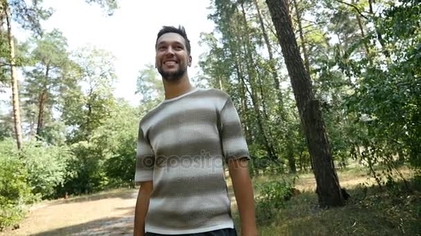 Um homem caucasiano barbudo está em uma floresta de pinheiros e sorri feliz em câmera lenta — Vídeo de Stock