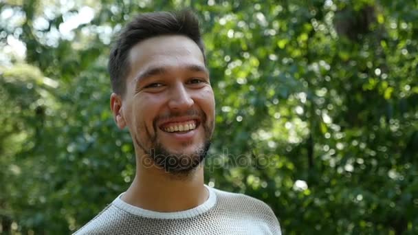 Een vrolijke bebaarde man glimlacht in een dennenbos in de zomer in slow motion — Stockvideo